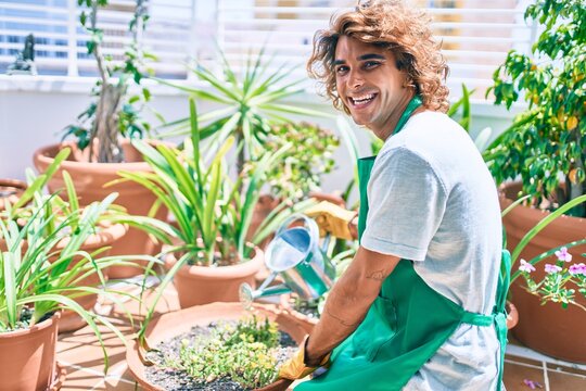 Young hispanic gardener smiling happy caring plants using watering can at terrace