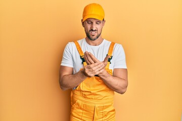 Young handsome man wearing handyman uniform over yellow background suffering pain on hands and fingers, arthritis inflammation