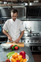 Fototapeta na wymiar Young professional chef in uniform cutting fresh onion and other vegetables