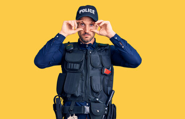 Young handsome man wearing police uniform trying to open eyes with fingers, sleepy and tired for...
