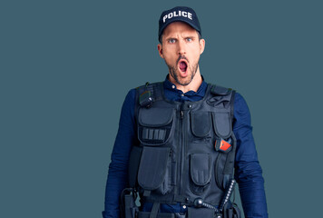 Young handsome man wearing police uniform in shock face, looking skeptical and sarcastic, surprised with open mouth