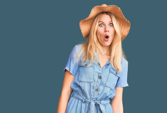 Young beautiful blonde woman wearing summer hat and dress afraid and shocked with surprise expression, fear and excited face.