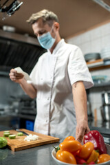 Contemporary young chef in uniform and protective mask taking bowl with capsicum