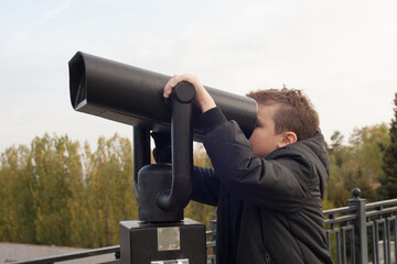 Fototapeta na wymiar a boy with a black jacket on the observation deck looks through binoculars