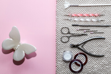 Set of tools for manicure and nail design with powder on towel with a white pearl butterfly candle on light pink background
