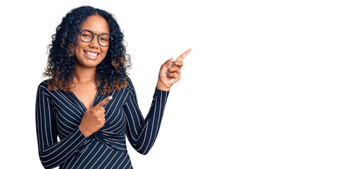 Young african american woman wearing casual clothes and glasses smiling and looking at the camera pointing with two hands and fingers to the side.