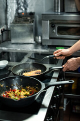 Hands of male chef roasting piece of salmon while cooking fish and vegetables