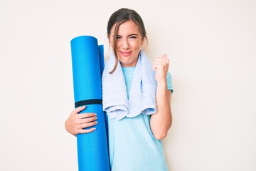 Beautiful young caucasian woman holding yoga mat annoyed and frustrated shouting with anger, yelling crazy with anger and hand raised