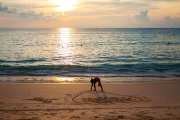 girl painting heart on sand on beach near the sea in sunset
