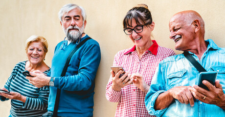 Happy senior friends having fun with modern smart phones - Retired people sharing content online with mobile cellphone - Positive elderly lifestyle concept with focus on woman with eyeglasses