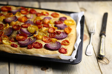 Fresh homemade focaccia on a pan with tomatoes and blue onions. Italian cuisine at home. Focaccia recipe.