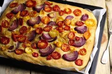 Fresh homemade focaccia on a pan with tomatoes and blue onions. Italian cuisine at home. Focaccia recipe.