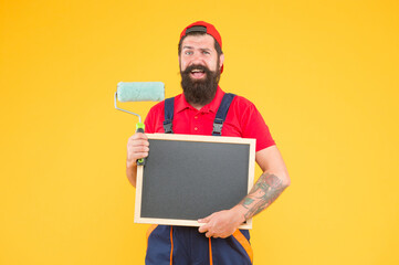 Ready to work. creative idea. foreman advertises the service of wall facing. happy man with board copy space. mature hipster use paint roller tool for painting. repairman or builder working