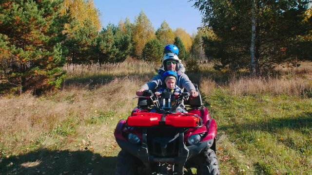 A man with his kids rides quad bikes in the autumn field