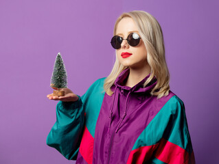 Style blonde in 80s windbreaker and roud sunglasses with Christmas tree