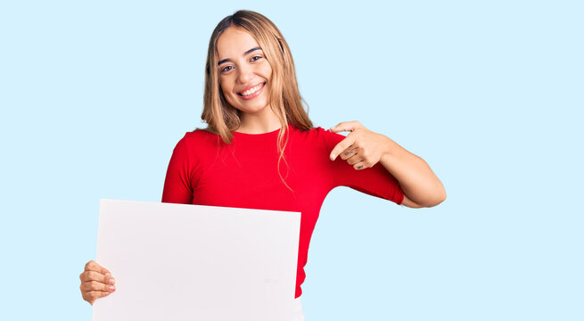 Young beautiful blonde woman holding blank empty banner smiling happy pointing with hand and finger