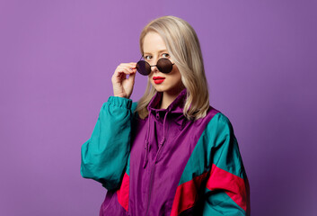 Style blonde in 80s windbreaker and roud sunglasses on purple background