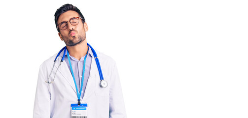 Young hispanic man wearing doctor uniform and stethoscope looking at the camera blowing a kiss on...