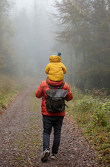 father and son are walking in the autumn forest in fog.