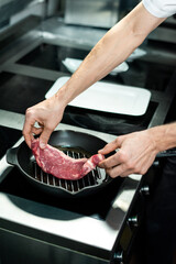 Hands of young chef putting piece of meat on grill frying pan with vegetable oil