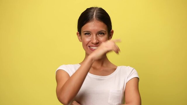 sexy casual woman smiling at the camera, crossing her arms, pointing at the camera on yellow background