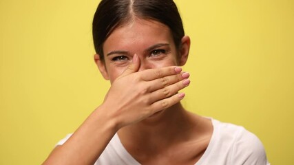close up on a beautiful casual woman laughing, covering her mouth and gesturing that she can't take it anymore on yellow background