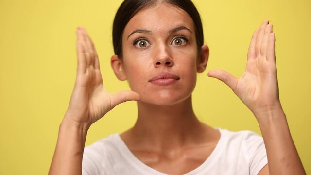 close up on a young casual woman looking aside, mimicking with her hands that are babbling around and make her desperate on yellow background