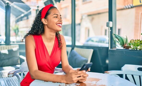 Young african american girl smiling happy using smartphone sitting on the table at coffee shop terrace.