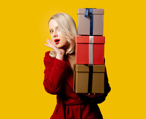 Blonde woman in red coat with gift boxes on yellow background