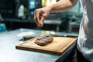 Hand of chef sprinkling spices on roasted beef steak during preparation