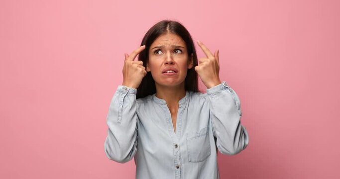 young casual woman in blue denim shirt having a superior attitude, making faces, pointing fingers to temples and inviting to think, making bla bla bla gestures, looking around and refusing on pink