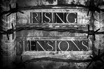 Rising Tensions text formed with real authentic typeset letters surrounded by barbed wire on vintage textured monochrome background
