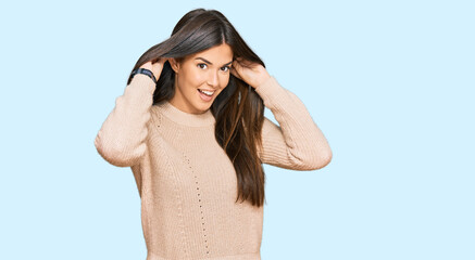 Young brunette woman wearing casual winter sweater smiling pulling ears with fingers, funny...