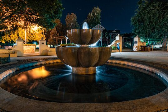 Plaza fountain springs water over a reflective surface at Ojai park under stars in the night sky.