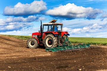 Agriculture red tractor cultivating field over blue sky. Old red tractor in the agricultural field; mechanism. Tractor plowing land. Harvester sowing wheat.