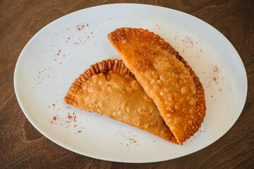 National cuisine. Fried cheburek with meat. Minced meat pie on a white plate on a dark wooden background