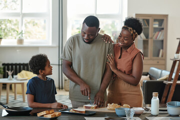 Young African man preparing sandwiches for breakfast between his wife and son