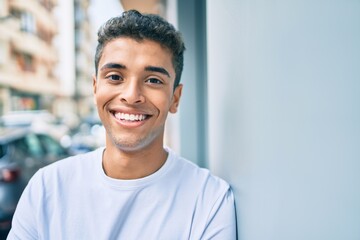 Obraz premium Young latin man smiling happy leaning on the wall at the city.