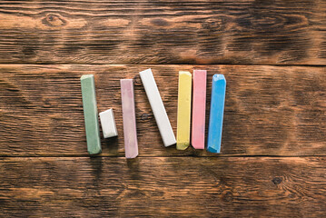 Colorful chalks on the brown wooden desk background.