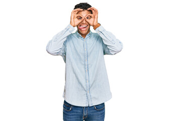 Young handsome african american man wearing casual clothes doing ok gesture like binoculars sticking tongue out, eyes looking through fingers. crazy expression.