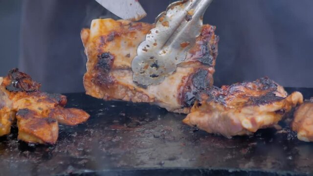 Slow motion: chef holding knife, cutting prepared juicy meat steaks on brazier with hot flame at summer local food market - close up view. Outdoor cooking, gastronomy, cookery, street food concept