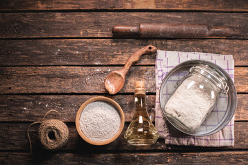 Flour in a jar, sifter, plunger and cooking oil on the kitchen table background.