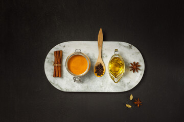Spices for Golden milk. Ingredients for making a paste from turmeric powder, oil, black pepper and spices. Top view on a black background