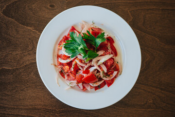Vegetarian salad of tomatoes and onions with herbs on a white plate. The dish stands on a dark wooden background. Healthy eating. Diet