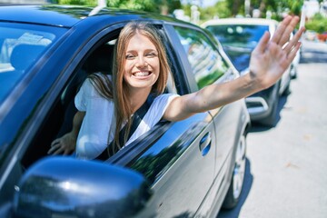 Young beautiful blonde woman smiling happy sitting at the car with hand out and cheerful expression