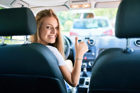Young beautiful blonde woman smiling happy driving car with thumb up doing ok sign.
