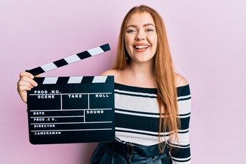 Young beautiful redhead woman holding video film clapboard looking positive and happy standing and...