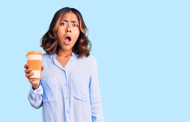 Young beautiful mixed race woman drinking a coffee from take away cup scared and amazed with open mouth for surprise, disbelief face