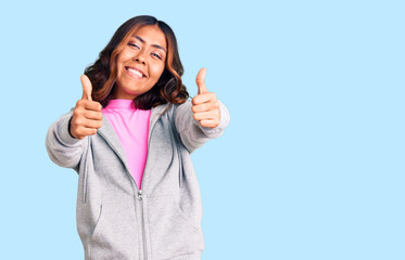 Young beautiful mixed race woman wearing casual sporty clothes approving doing positive gesture with hand, thumbs up smiling and happy for success. winner gesture.