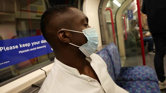 Black male on underground tube wearing face mask 